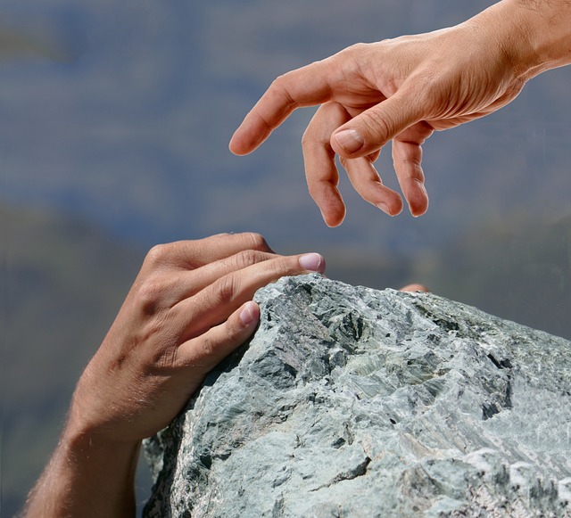 a hand hanging onto a cliff edge while another hand reaches out to help