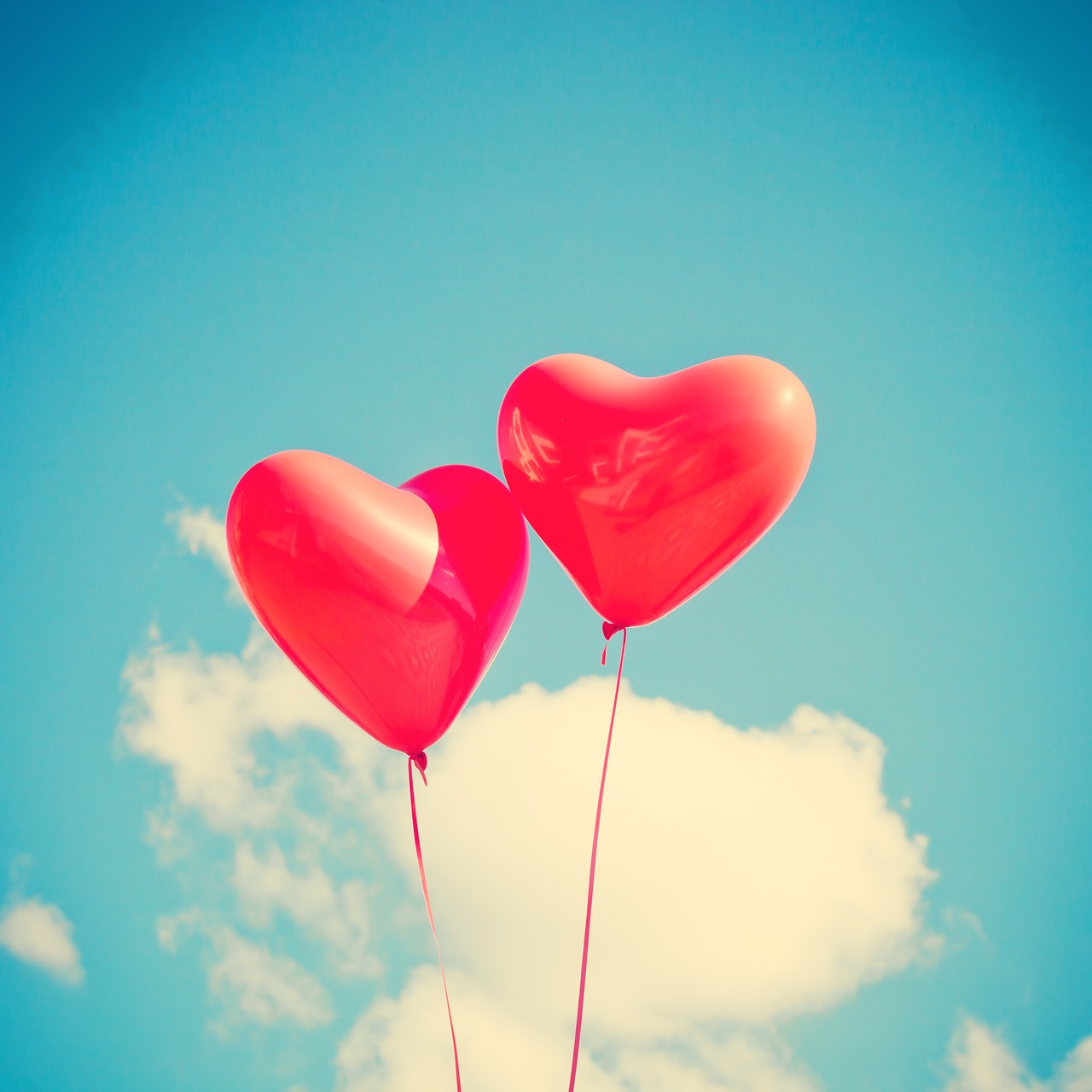 two Hot pink heart shaped balloons floating in the beautiful bright blue summer sky with one and a half clouds near the bottom of the frame the one on the left slightly shorter than the other reprsenting Evelyn