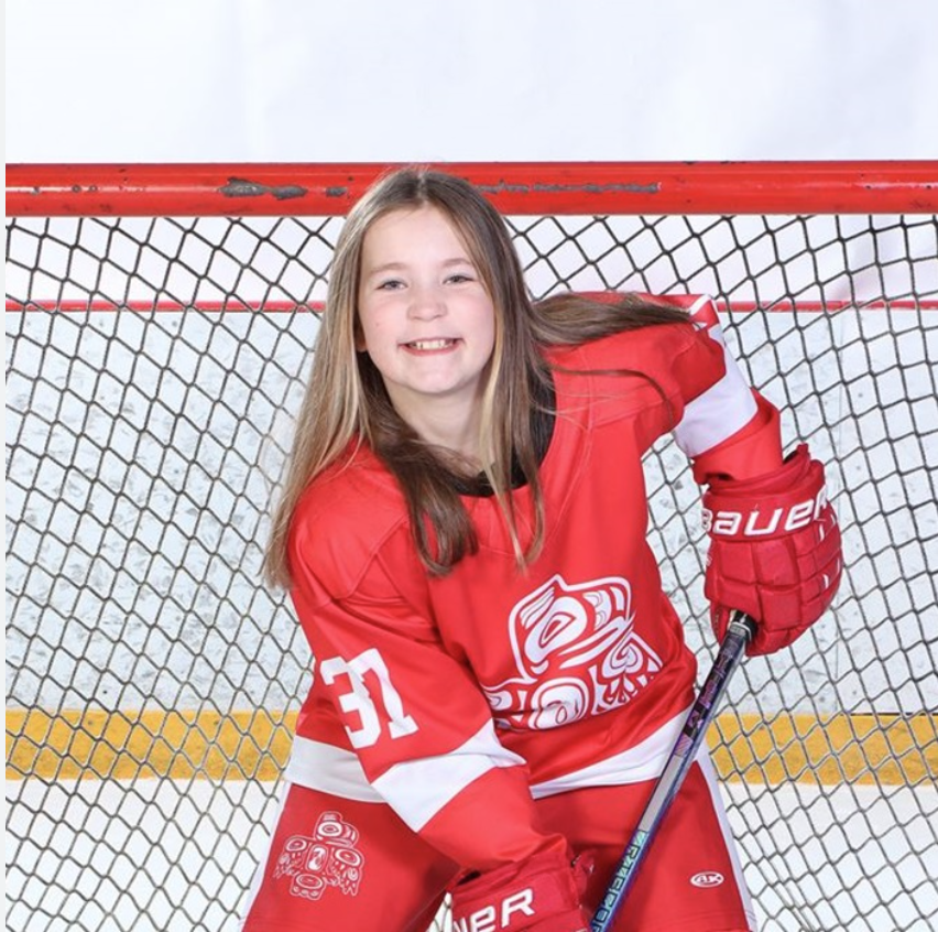 Lexi in a photo with hockey gear in infront of a hockey net