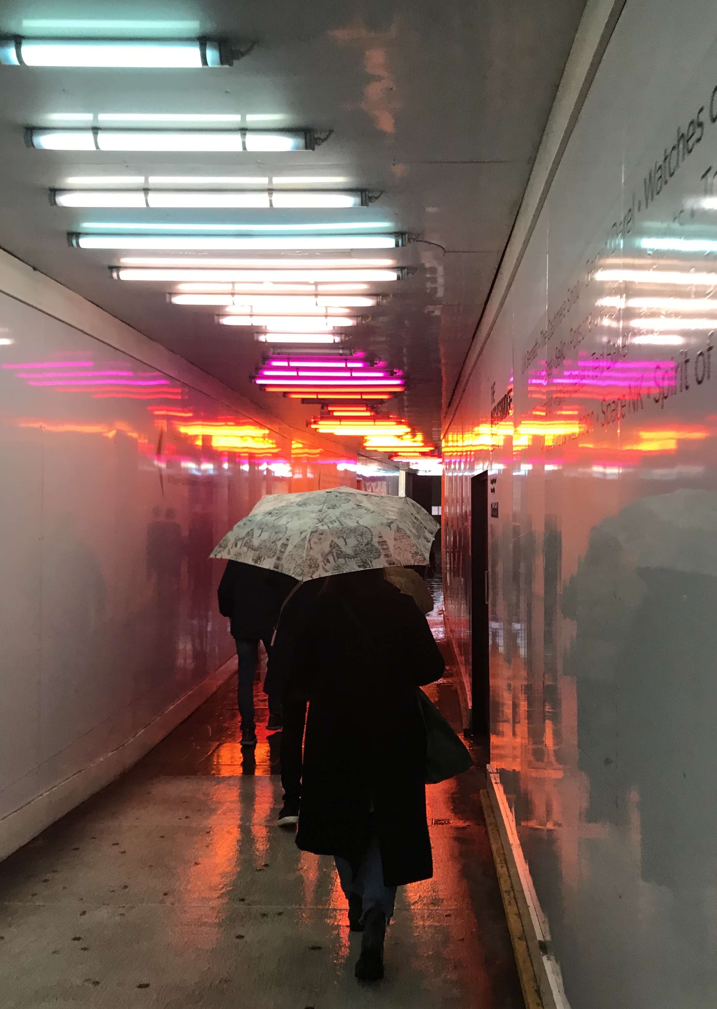 woman walking in London with umbrella under neon lights
