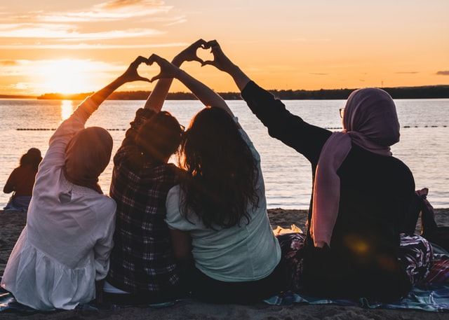 Image of friends making hearts with their hands sitting on shore